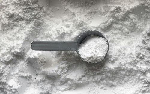 Fine white powder being scooped for gravimetric dosing